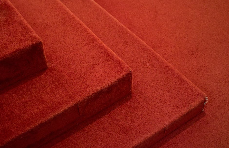 The image features a spacious, vintage-style interior hallway with a rich red patterned carpet covering the floor, which appears clean and well-maintained. The walls are paneled with wood and painted